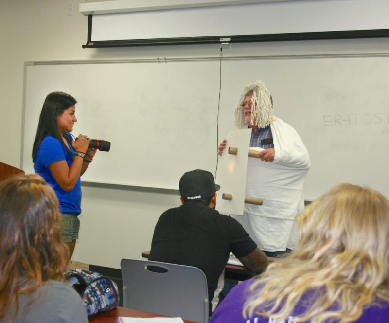 A HISTORY LESSON Eratosthenes of Cyrene, the Greek scientific writer, astronomer, and poet, who made the first measurement of the size of Earth for which any details are known, is being portrayed by U.S. History instructor Ken Hanushek in the History 1301 class at the PJC-Sulphur Springs Center. Shining a light on the subject is student Airy Osorio. Hanushek likes to bring his history subjects to life in class. “They are better understood that way,” he said.