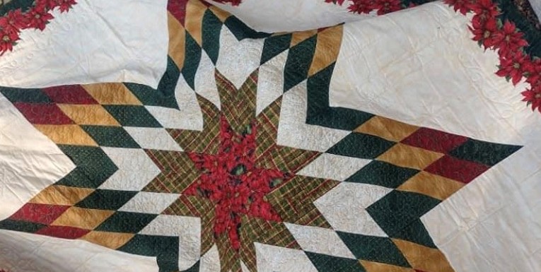 Christmas Star Quilt made by: Cara Duncan. Full size 79” x 79”. Dark green back, front has Christmas Star trimmed with Poinsettias - Donated by Bill & Beverley Owens