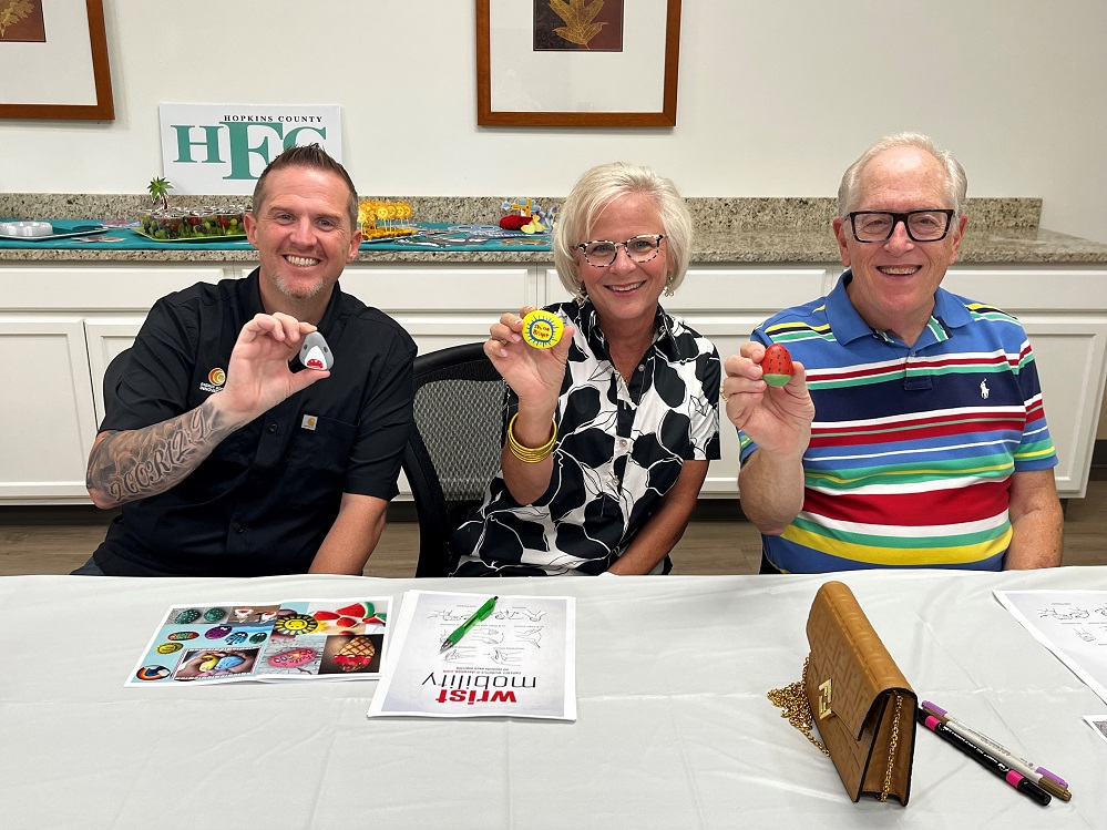 Hopkins County Health Care Foundation Board Members Kenny Rogers, Pam Black, and Bob Weaver flash their smiles and their rock paintings. Rock painting was part of the Kick-Off of the Summer of Healthy Fun held on Monday, June 23.